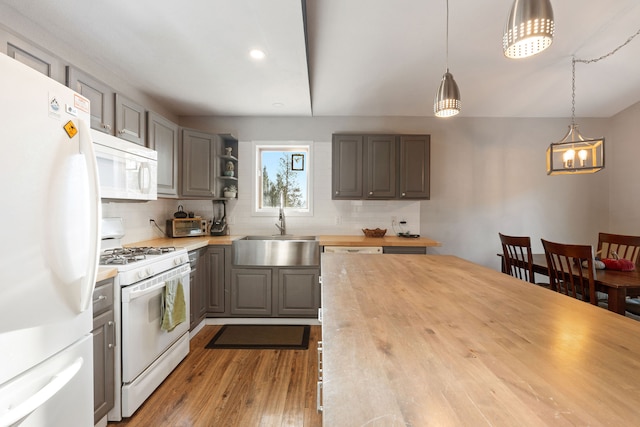 kitchen with pendant lighting, white appliances, backsplash, sink, and hardwood / wood-style flooring