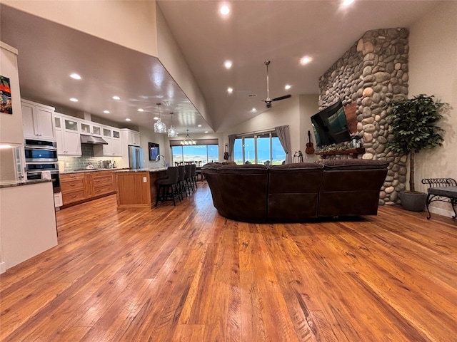 living room with a fireplace, light hardwood / wood-style floors, lofted ceiling, and ceiling fan with notable chandelier