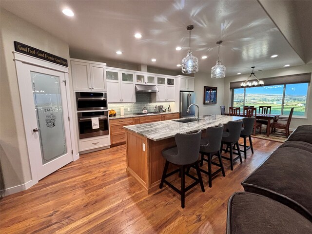 kitchen featuring white cabinets, a large island with sink, decorative light fixtures, and light stone counters