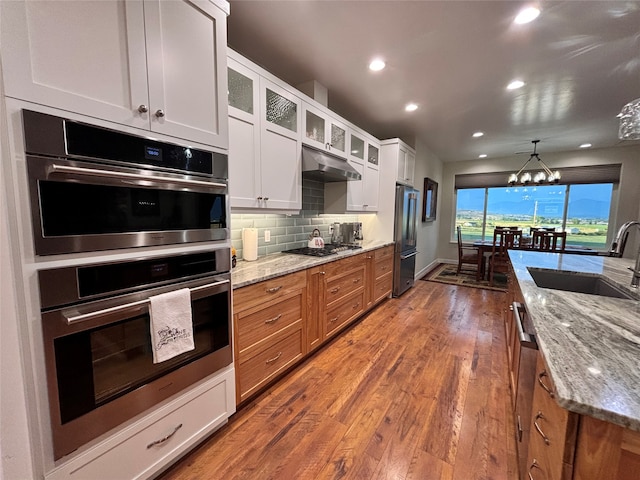 kitchen with light stone counters, stainless steel appliances, hardwood / wood-style floors, sink, and white cabinets