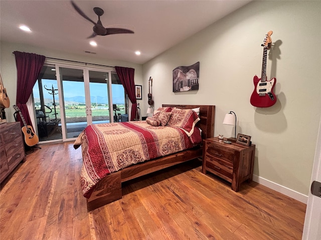 bedroom with a mountain view, access to outside, wood-type flooring, and ceiling fan