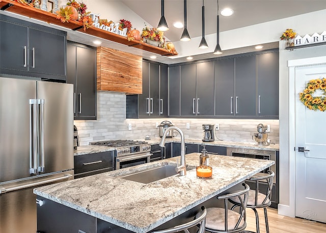 kitchen featuring hanging light fixtures, a breakfast bar area, an island with sink, high quality appliances, and light stone countertops