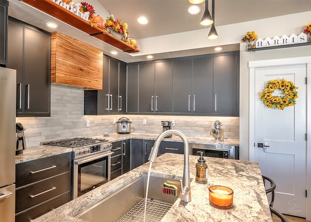 kitchen with stainless steel stove, decorative light fixtures, light stone counters, and tasteful backsplash