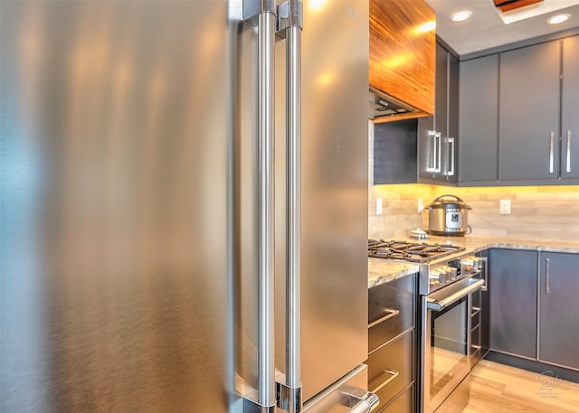 kitchen featuring premium appliances, light stone counters, tasteful backsplash, gray cabinets, and light wood-type flooring