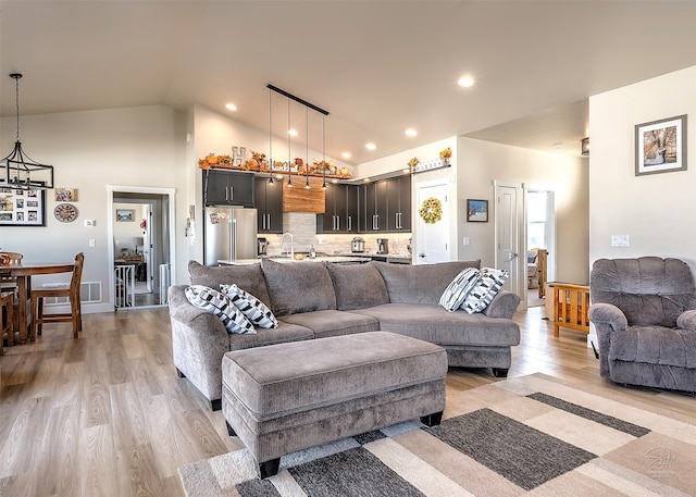 living room featuring light wood-type flooring, a chandelier, sink, and high vaulted ceiling