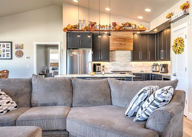 kitchen featuring tasteful backsplash, light wood-type flooring, light stone countertops, hanging light fixtures, and high quality fridge