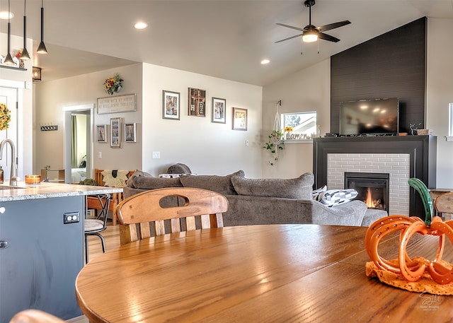 dining area featuring lofted ceiling, sink, ceiling fan, and a brick fireplace