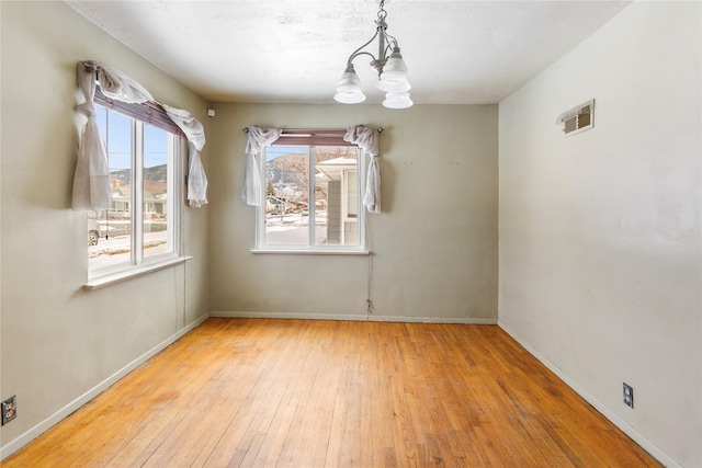 unfurnished dining area featuring hardwood / wood-style flooring, visible vents, a chandelier, and baseboards