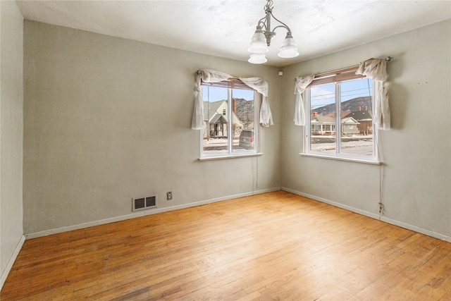 unfurnished room with an inviting chandelier, baseboards, visible vents, and hardwood / wood-style floors