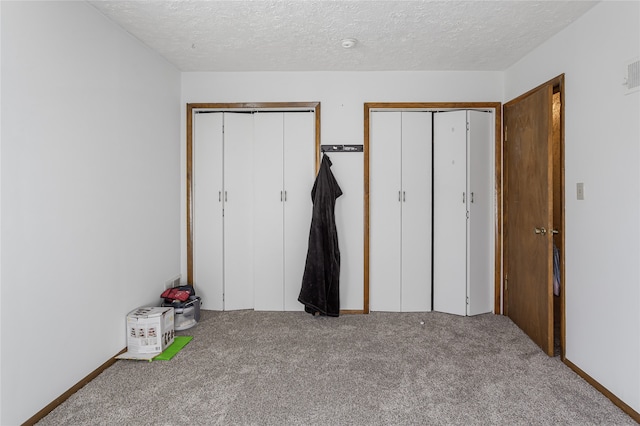 unfurnished bedroom featuring two closets, a textured ceiling, and carpet floors