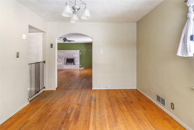 spare room with visible vents, arched walkways, hardwood / wood-style flooring, a fireplace, and ceiling fan with notable chandelier