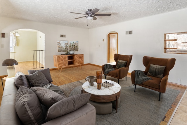 living room featuring visible vents, arched walkways, light wood-style flooring, and a textured ceiling