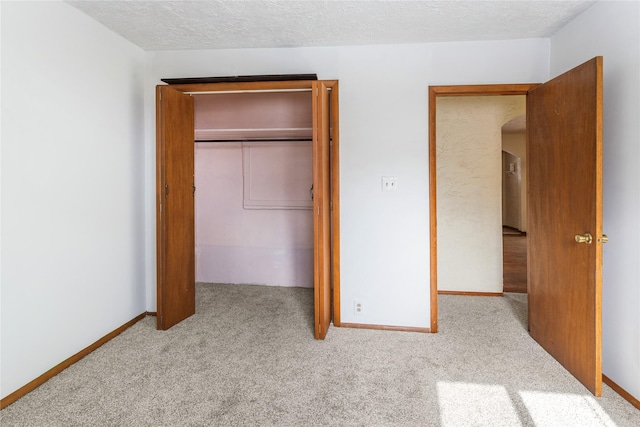 unfurnished bedroom featuring carpet floors, a closet, a textured ceiling, and baseboards