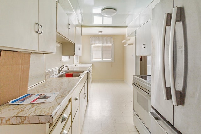 kitchen with white cabinets, freestanding refrigerator, light countertops, a sink, and range with electric stovetop