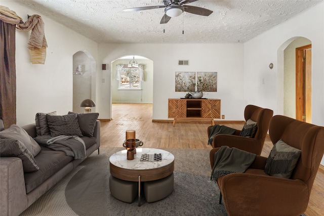 living area with arched walkways, ceiling fan, a textured ceiling, wood finished floors, and visible vents