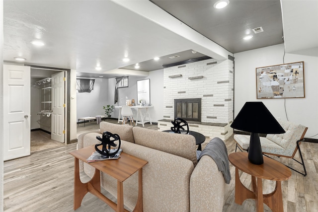 living room featuring light wood-type flooring, a brick fireplace, visible vents, and recessed lighting