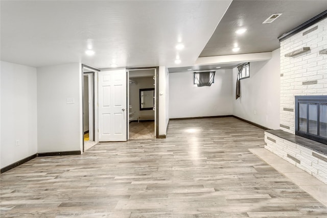 finished basement with visible vents, a brick fireplace, light wood-style flooring, and baseboards