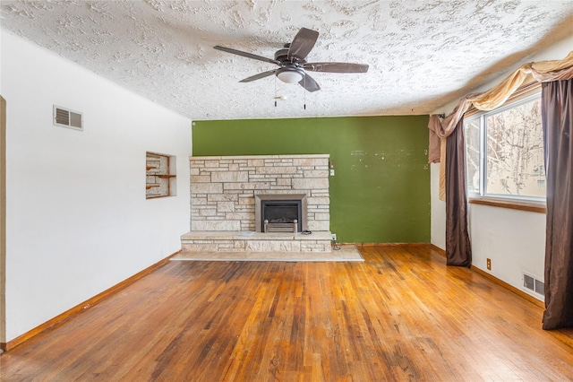 unfurnished living room with wood-type flooring, visible vents, and a stone fireplace