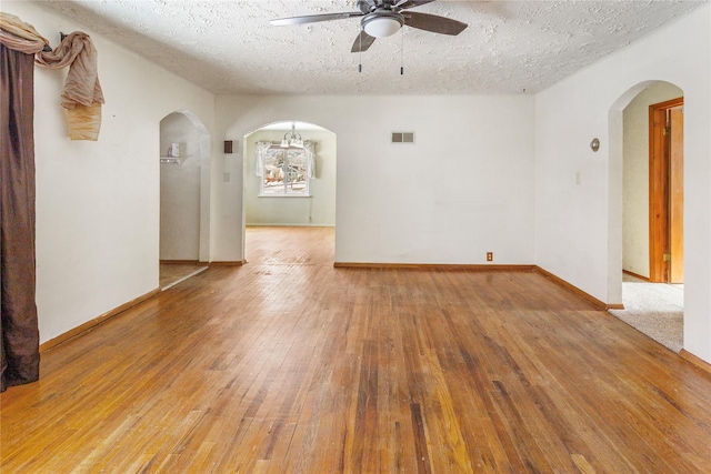 spare room with visible vents, arched walkways, a ceiling fan, wood-type flooring, and a textured ceiling