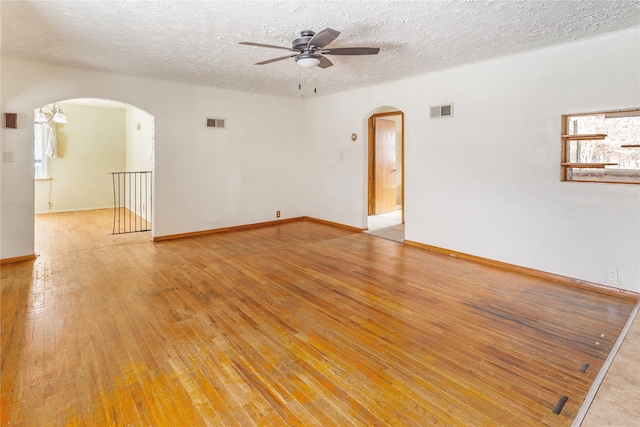 empty room with light wood-type flooring, arched walkways, and visible vents