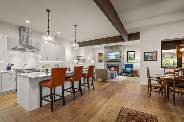 kitchen with light hardwood / wood-style floors, a center island, white cabinets, wall chimney exhaust hood, and beam ceiling