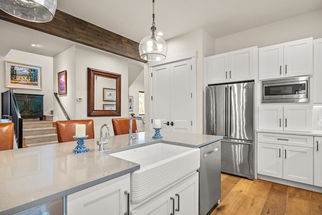 kitchen featuring stainless steel appliances, white cabinetry, hanging light fixtures, sink, and light hardwood / wood-style floors