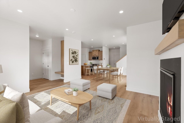 living room featuring a warm lit fireplace, light wood finished floors, recessed lighting, and baseboards