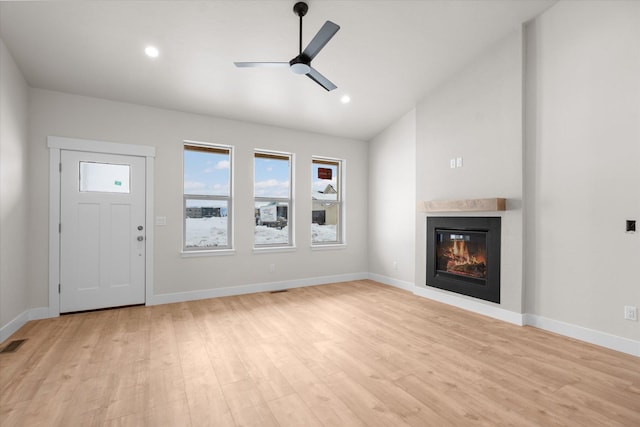 unfurnished living room with light wood-style flooring, a glass covered fireplace, a ceiling fan, and baseboards