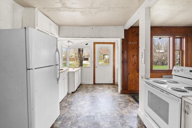 1312 2nd Ave E, Kalispell, MT 59901 - kitchen with white appliances, white cabinets, stone finish floors, light countertops, and wood walls