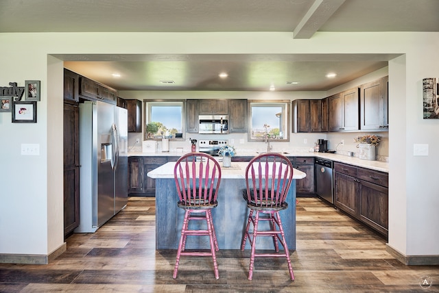 kitchen with a kitchen bar, hardwood / wood-style floors, sink, a kitchen island, and appliances with stainless steel finishes