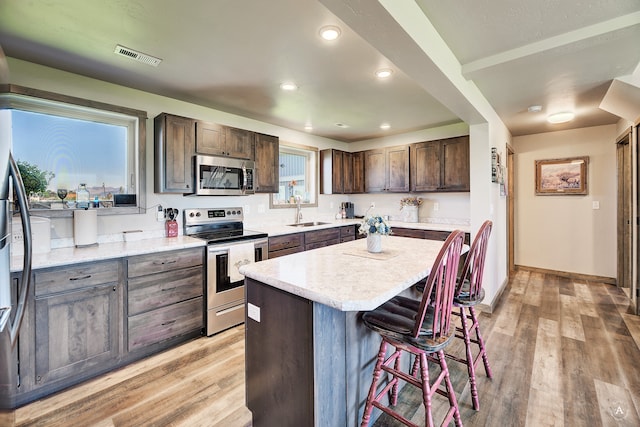 kitchen featuring stainless steel appliances, dark brown cabinetry, sink, a center island, and light wood-type flooring