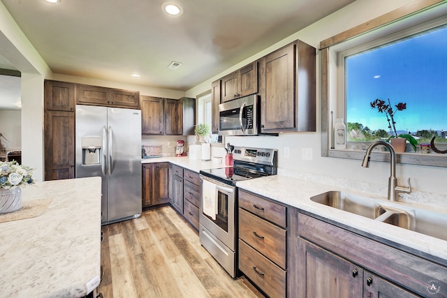 kitchen with light stone counters, appliances with stainless steel finishes, dark brown cabinets, sink, and light hardwood / wood-style flooring