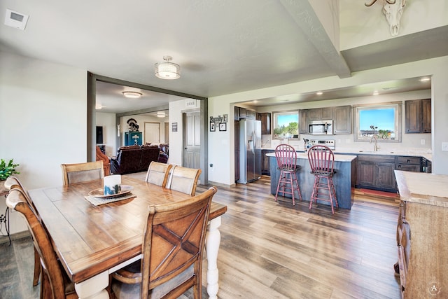 dining room featuring beamed ceiling, sink, and light hardwood / wood-style floors