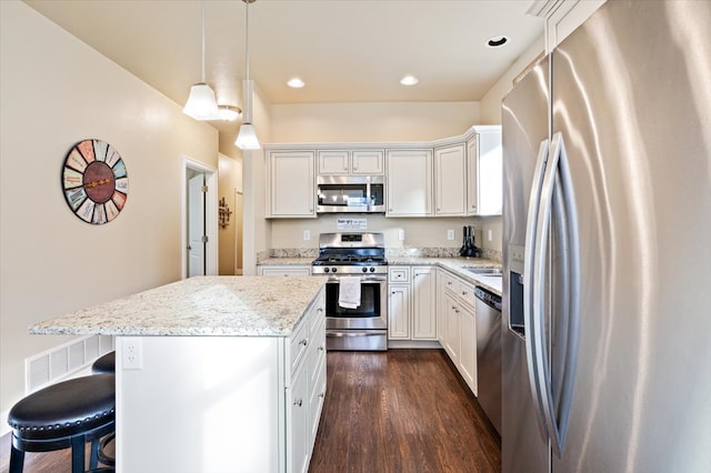 kitchen with appliances with stainless steel finishes, pendant lighting, white cabinetry, a center island, and light stone countertops