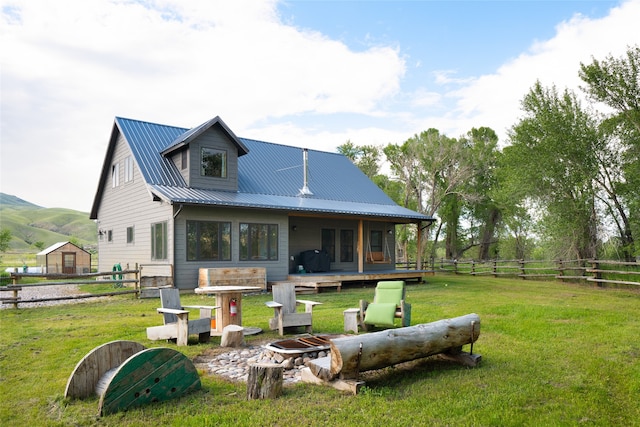 rear view of property featuring a lawn, a deck with mountain view, and a fire pit