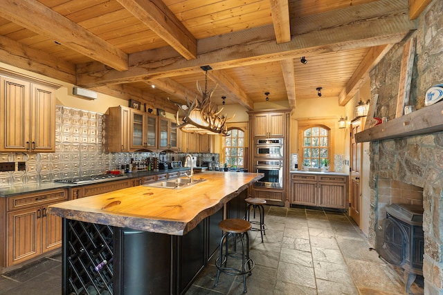 kitchen with wood counters, decorative backsplash, a center island with sink, and stainless steel appliances