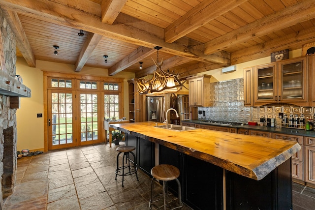 kitchen with sink, a kitchen island with sink, beamed ceiling, butcher block countertops, and decorative backsplash