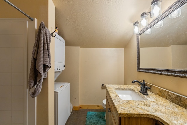 bathroom featuring a tile shower, tile patterned flooring, toilet, vanity, and stacked washer and clothes dryer