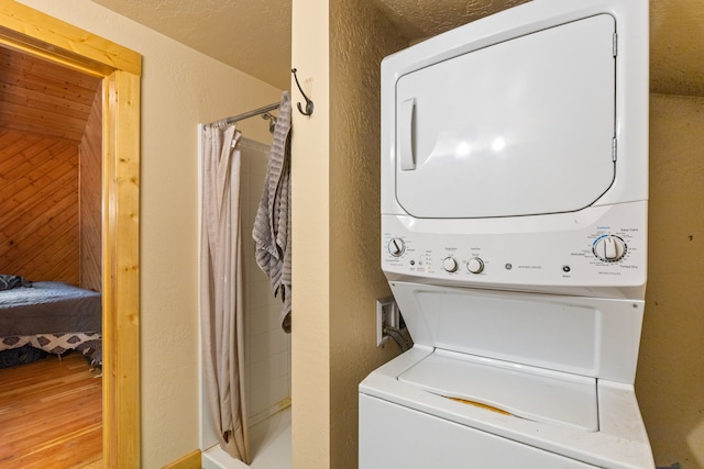 laundry area featuring stacked washer / dryer, light hardwood / wood-style flooring, and a textured ceiling