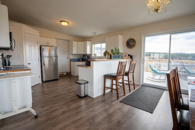 kitchen with kitchen peninsula, dark hardwood / wood-style flooring, stainless steel appliances, white cabinets, and a breakfast bar area