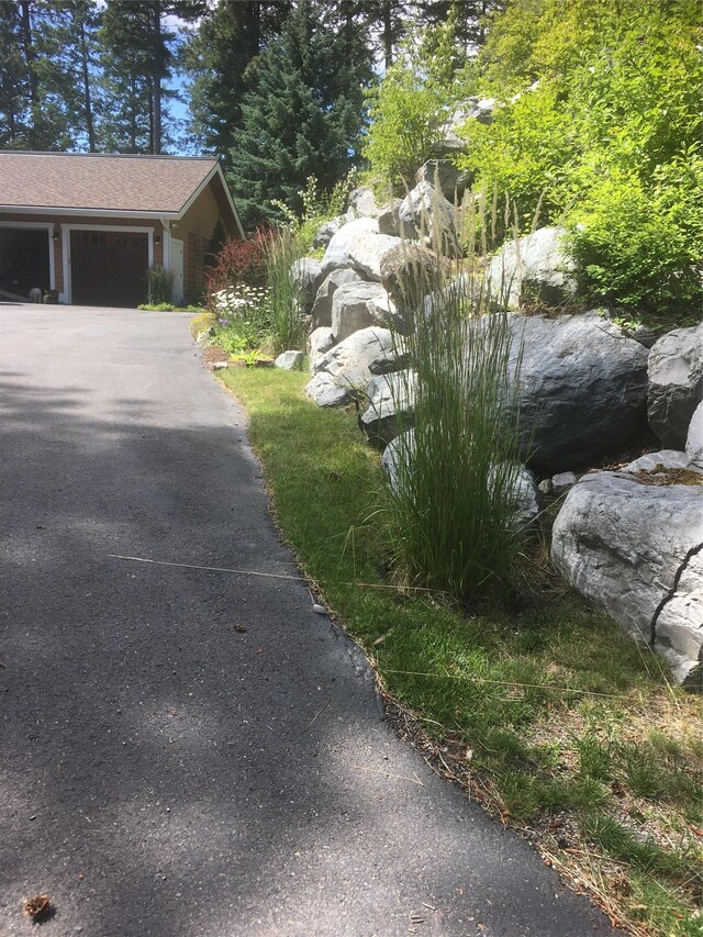 32054 Birch Tree Dr, Bigfork, MT 59911 - modern home with stone siding, asphalt driveway, a garage, and a chimney