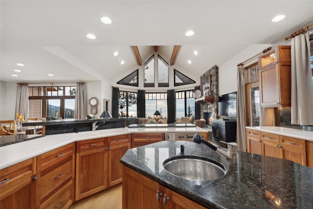 kitchen featuring lofted ceiling, dark stone counters, sink, light wood-type flooring, and a fireplace