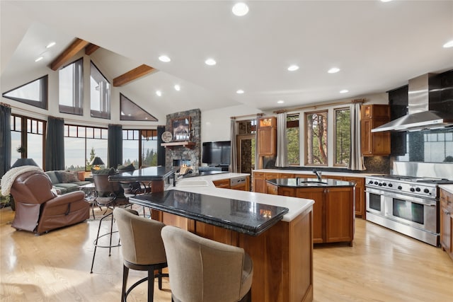 kitchen featuring beam ceiling, a center island, wall chimney range hood, light hardwood / wood-style flooring, and double oven range