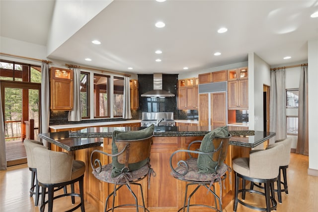 kitchen featuring a breakfast bar, backsplash, paneled built in fridge, light hardwood / wood-style flooring, and wall chimney exhaust hood