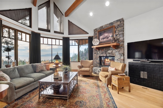 living room featuring beamed ceiling, wood-type flooring, a fireplace, and a wealth of natural light