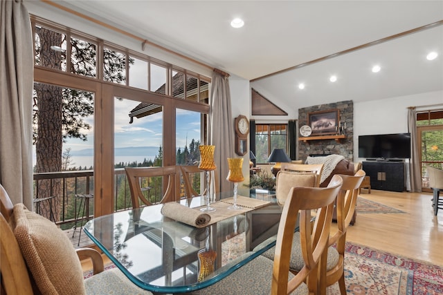 dining area with a stone fireplace, light hardwood / wood-style flooring, and vaulted ceiling