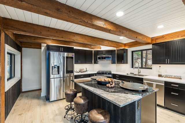 kitchen featuring stainless steel appliances, sink, beam ceiling, a kitchen island, and a breakfast bar area