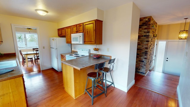 kitchen featuring a kitchen bar, kitchen peninsula, white appliances, wood-type flooring, and pendant lighting