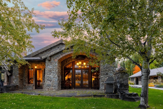 exterior entry at dusk featuring french doors and a lawn