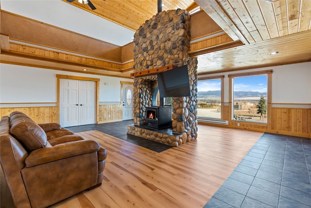 living room with hardwood / wood-style floors, a wood stove, wooden walls, a towering ceiling, and wood ceiling